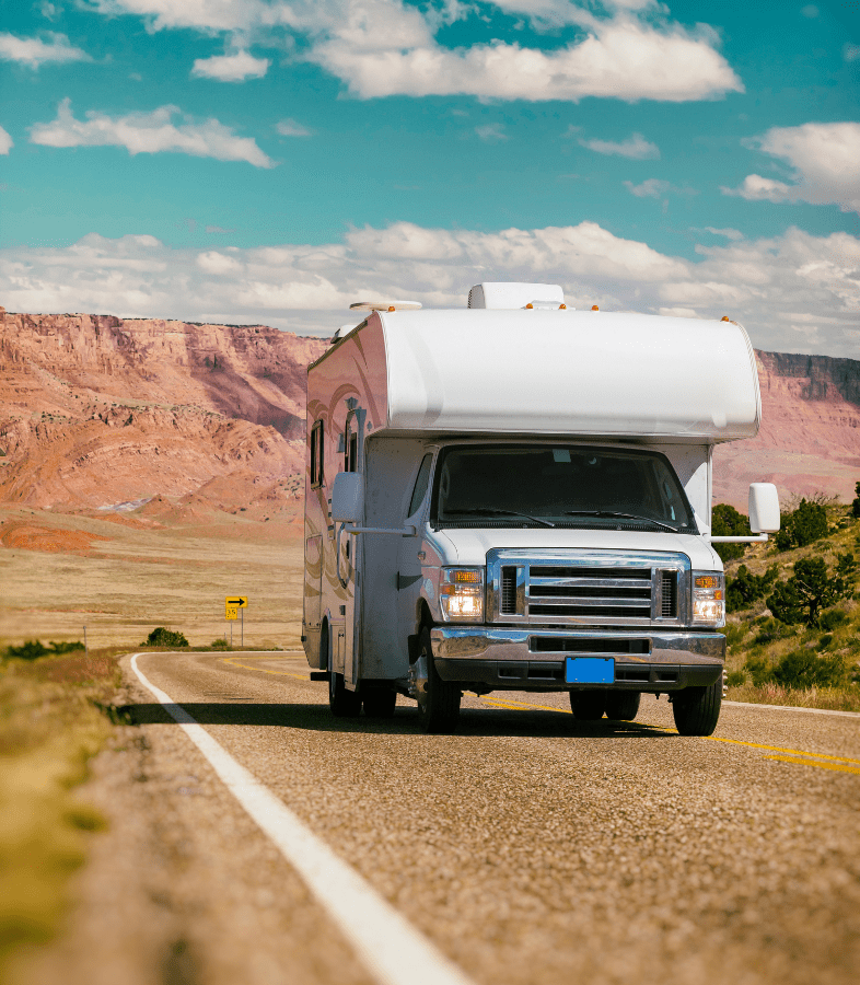 A moving white RV with the blue skies and clouds in the sky.